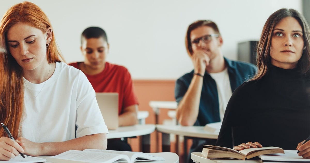 Vier Personen sitzen in zwei Reihen an Schreibtischen